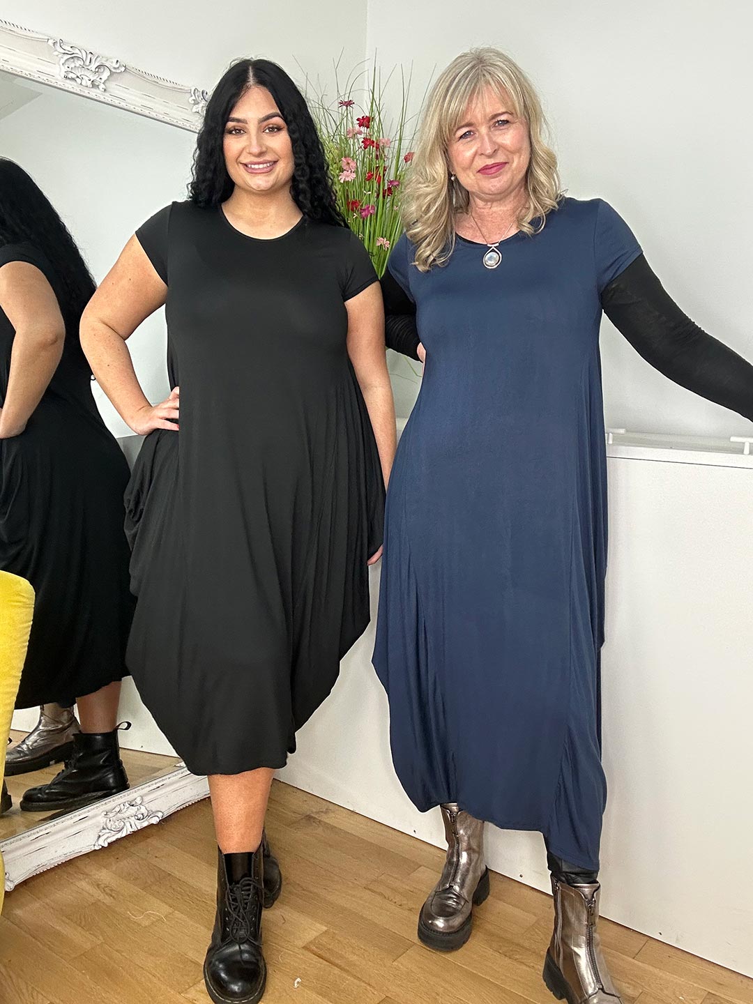 two women together, one wearing a black dress and the other a blue dress