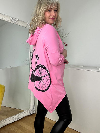 A woman in a pink top and black leggings stands in a cozy room, smiling confidently.