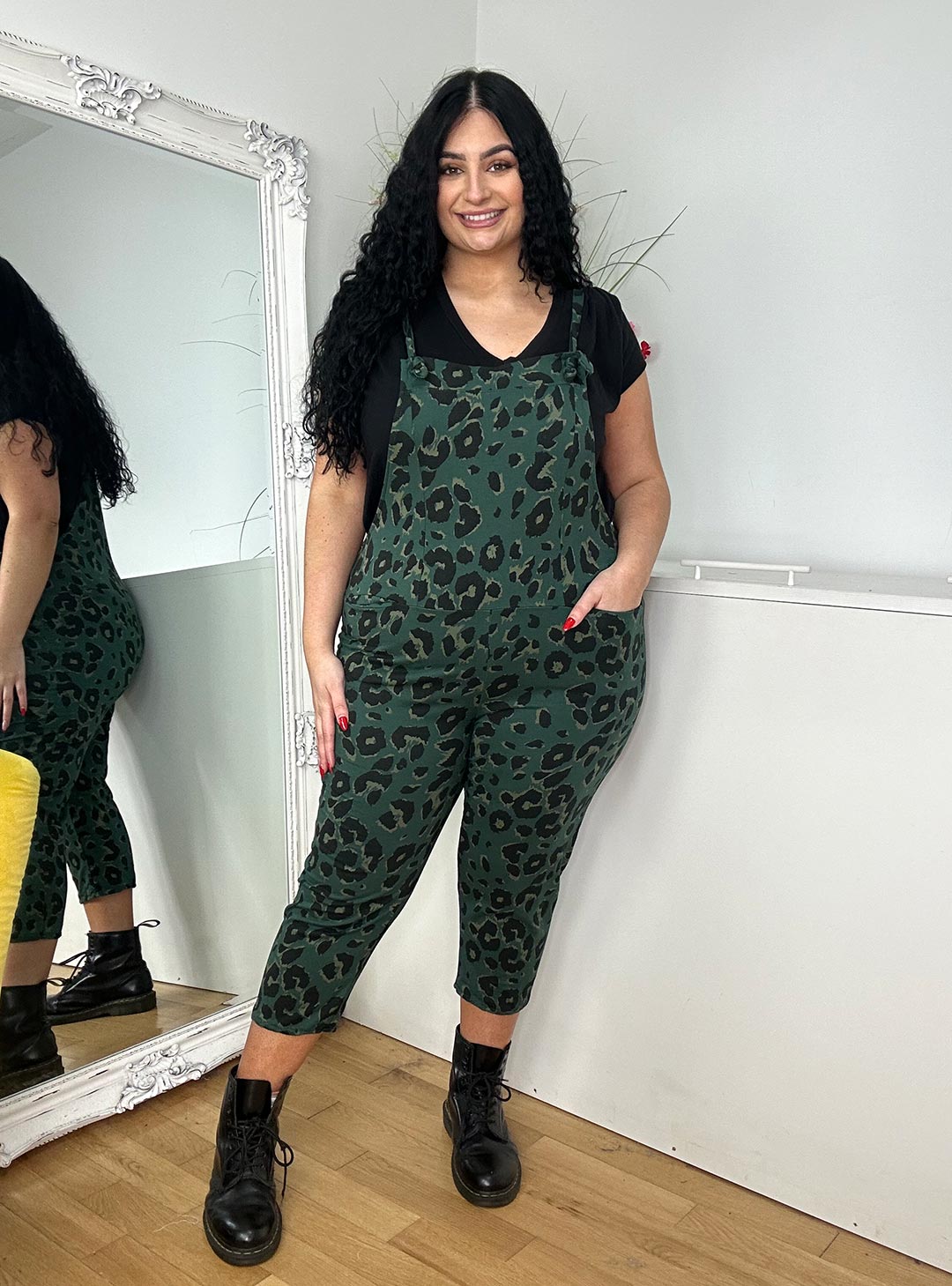 A woman wearing green leopard print overalls paired with a black top, showcasing a bold and stylish fashion choice.