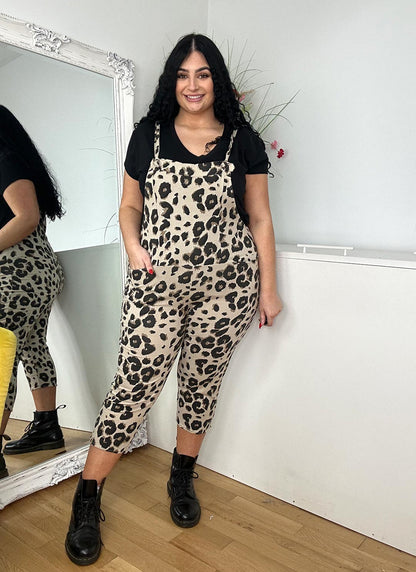 A woman wearing beige leopard print dungarees poses confidently in front of a mirror, showcasing her stylish outfit.