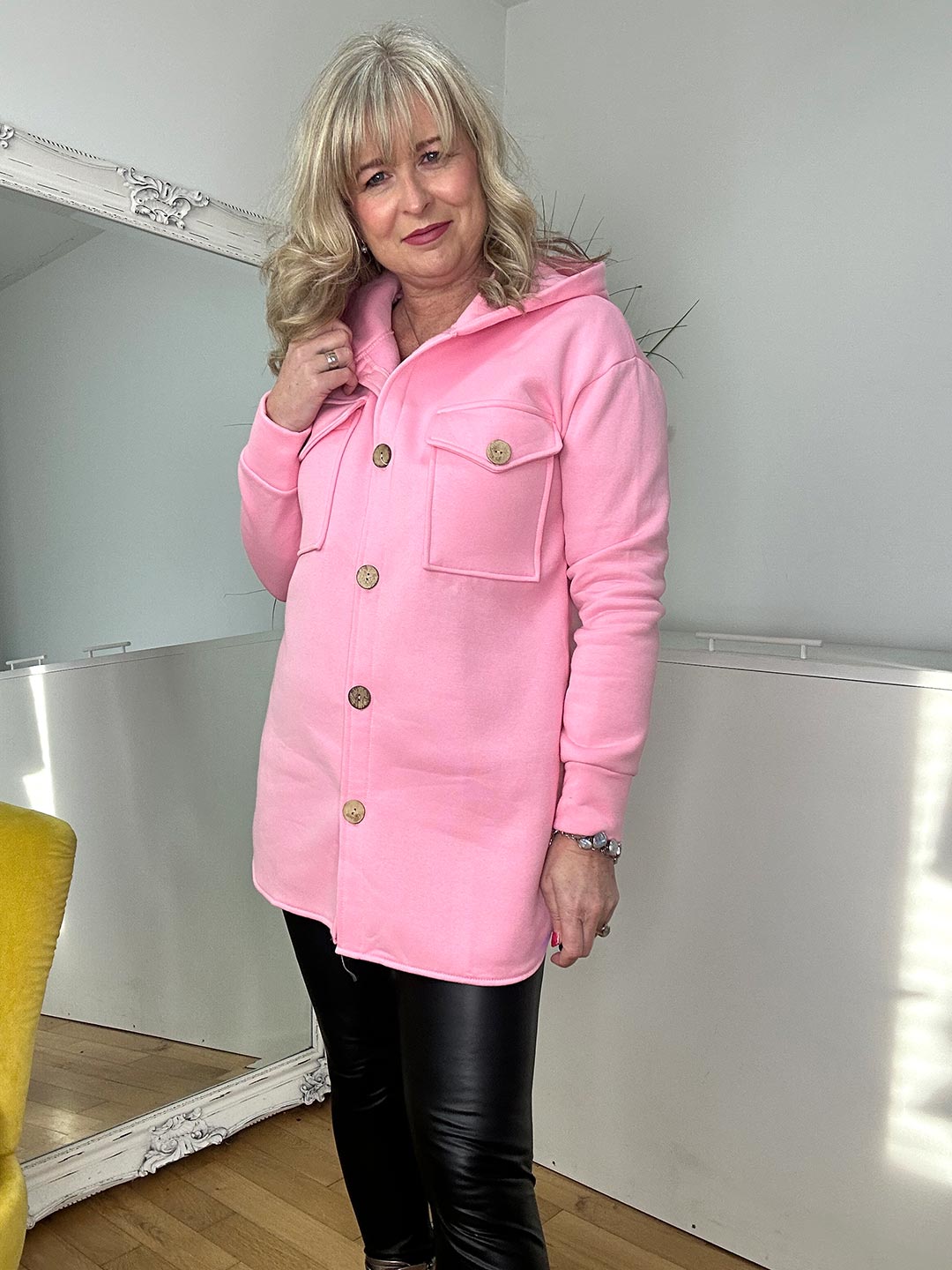 A woman in a pink jacket and black pants smiles, embodying a chic and contemporary look.