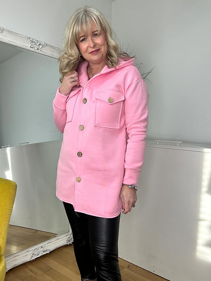 A woman in a pink jacket and black pants smiles, embodying a chic and contemporary look.