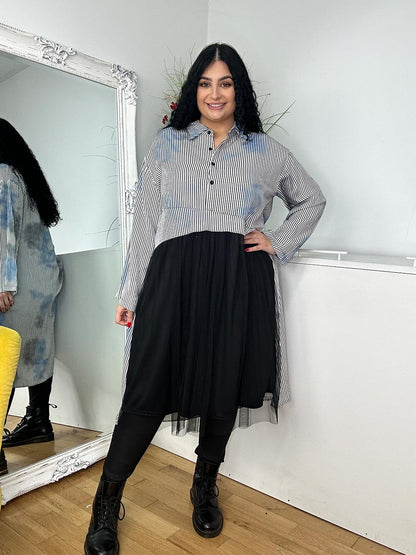 A woman wearing a grey shirt dress and black boots stands confidently, showcasing a stylish and modern outfit.