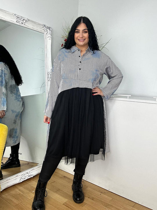 A woman wearing a grey shirt dress and black boots stands confidently, showcasing a stylish and modern outfit.