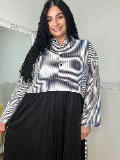 A woman wearing a grey shirt dress and black boots stands confidently, showcasing a stylish and modern outfit.