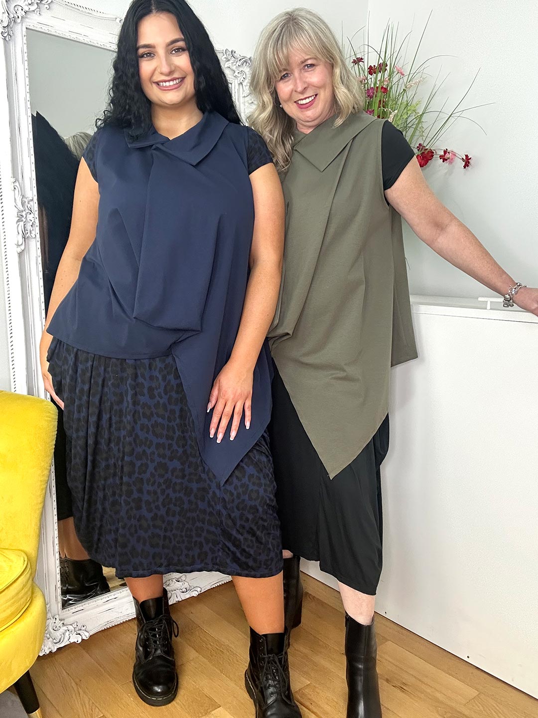  Two women pose in stylish outfits against a mirror, showcasing modern fashion.