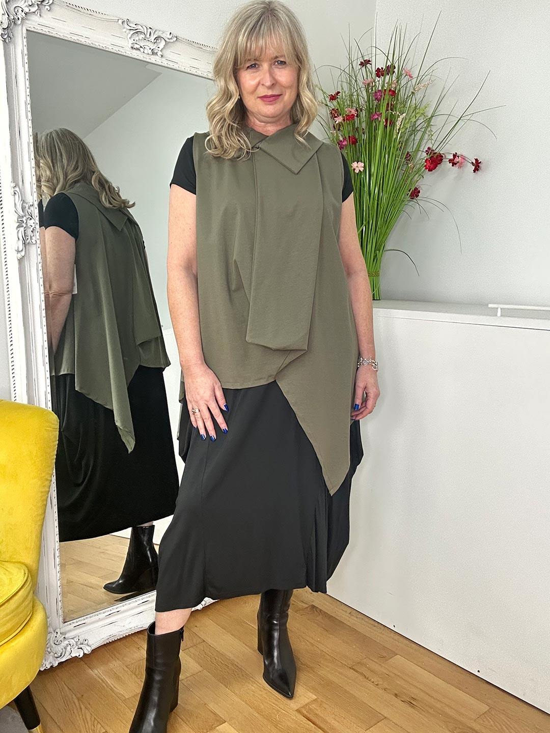 A woman in a black top and green vest, showcasing a modern and fashionable look against a simple backdrop