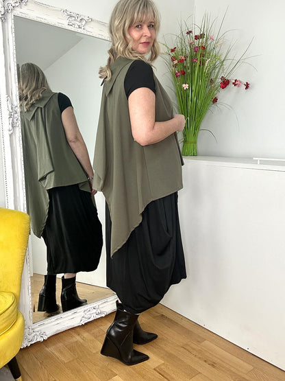 A woman in a black top and green vest, showcasing a modern and fashionable look against a simple backdrop